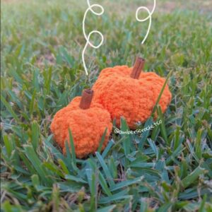 Crochet Pumpkin Plush on a grassy background with drawn wisps coming out of the stem, which is made of cinnamon sticks.